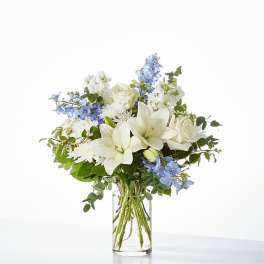 White lilies and roses with blue flowers in a clear glass vase