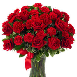 Arrangement of red roses and red carnations in a clear glass vase with a red ribbon