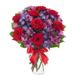 Arrangement of red roses, purple alstroemeria, and blue asters in a clear vase with a red bow.