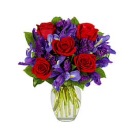 Red roses and purple irises arranged in a clear glass vase