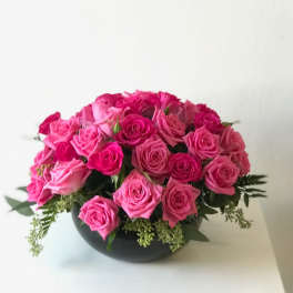 Low round arrangement of hot pink roses in a black bowl-shaped vase
