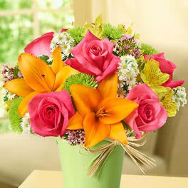 Bright arrangement of pink roses, orange lilies, and mixed blooms in a light green pail with a raffia bow