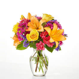 Bouquet of orange lilies, yellow roses, and pink daisies in a glass vase