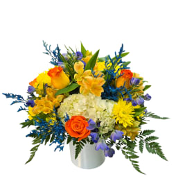 Bright mixed bouquet in a white vase with orange, yellow, blue, and purple flowers