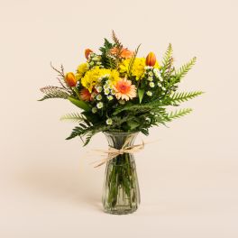 Mixed bouquet of yellow and peach flowers in a glass vase