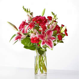 Bouquet of pink lilies, red roses, and carnations in a clear glass vase
