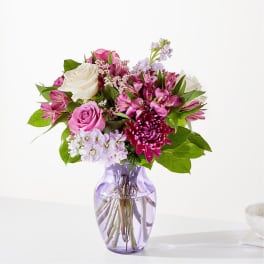Pink and white mixed flower bouquet in a purple glass vase