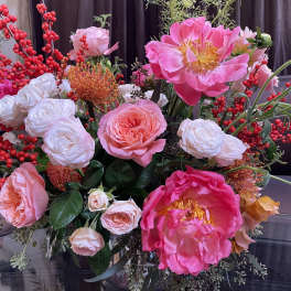 Pink and white floral arrangement with red berry branches in a glass vase