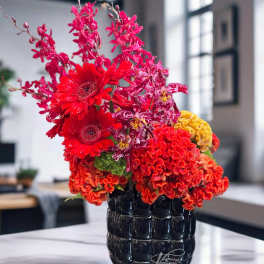 Bright red and pink floral arrangement in a black vase