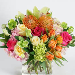 Mixed bouquet of roses, hydrangeas, and orange blooms in a glass vase