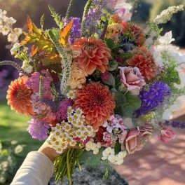 Handheld bouquet of orange, pink, purple, and white flowers