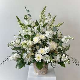 White floral arrangement in a woven basket with tall stems and greenery