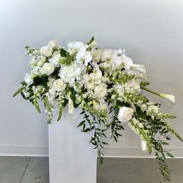 White floral arrangement with roses, orchids, and calla lilies on a pedestal