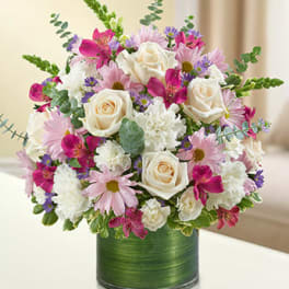 Round bouquet of cream roses, white carnations and pink daisies in a green-wrapped glass cylinder vase