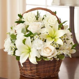 White lilies, roses, and carnations arranged in a brown wicker basket