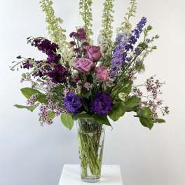 Tall mixed bouquet of purple, pink, and white flowers in a clear glass vase