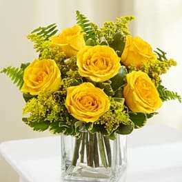 Yellow rose arrangement with small yellow filler flowers in a clear glass cube vase