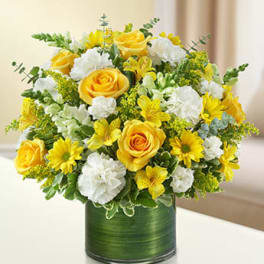 Round arrangement of yellow roses and daisies with white carnations in a glass cylinder vase