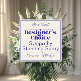 Standing sympathy spray with white lilies and greenery behind a sign