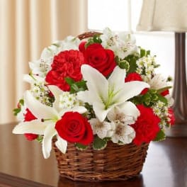 Red roses, red carnations, and white lilies arranged in a wicker basket on a table