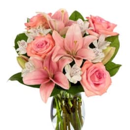 Pink lilies, roses, and white alstroemeria arranged in a clear glass vase