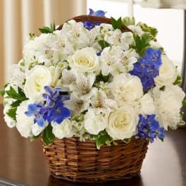 White roses, carnations, and alstroemeria with blue delphinium arranged in a wicker basket