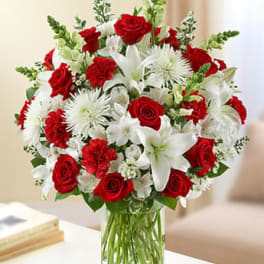 Arrangement of red roses, red carnations, and white lilies in a clear glass vase