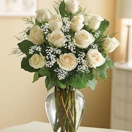 Arrangement of white roses with small white filler flowers in a clear glass vase