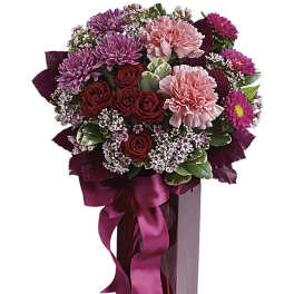 Bouquet of pink and red flowers in a tall glass vase with a ribbon