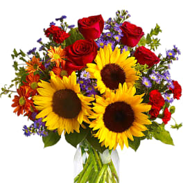 Bouquet of sunflowers, red roses, and purple daisies in a glass vase