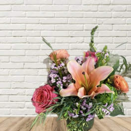Pink lilies and roses in a glass vase with purple filler flowers