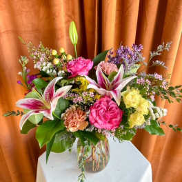 Bouquet of pink lilies, roses, and yellow blooms in a glass vase