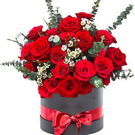 Red roses arranged in a black hatbox with a red ribbon