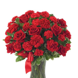 Red roses and carnations arranged in a clear glass vase with a red ribbon