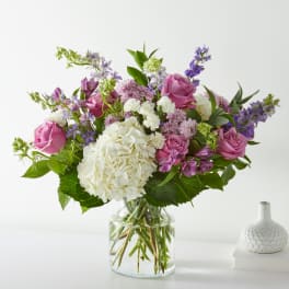 Bouquet of pink roses, white hydrangea, and purple flowers in a glass vase