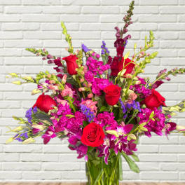 Bouquet of red roses, purple orchids, and pink snapdragons in a glass vase