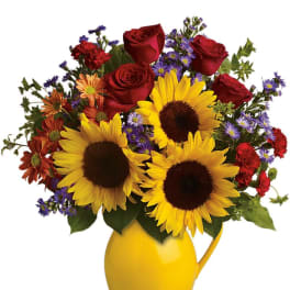 Bright bouquet of sunflowers, red roses, and mixed blooms in a yellow ceramic pitcher.