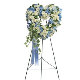 Heart-shaped standing wreath of white roses and blue hydrangeas on a metal easel with blue ribbon