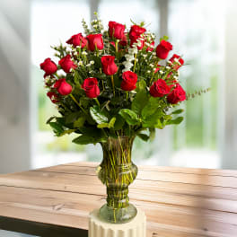 Red roses arranged in a clear glass vase with small white filler flowers.
