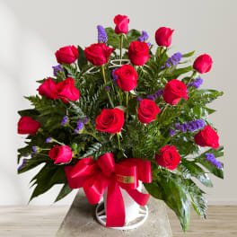 Red roses arranged in a white vase with a large red ribbon