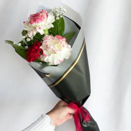Handheld bouquet of pink and white carnations wrapped in dark paper