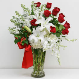 Red roses and white lilies in a clear glass vase with a red ribbon