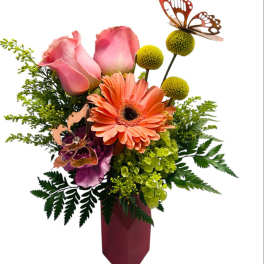 Pink roses and orange gerbera daisies in a burgundy vase with butterfly picks