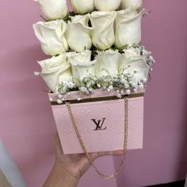 White roses arranged in a pink designer box with a gold chain handle