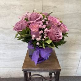 Pink roses in a purple vase with a ribbon bow