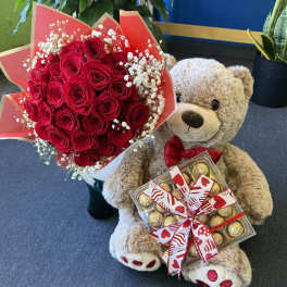 Red rose bouquet with baby’s breath beside a teddy bear holding chocolates
