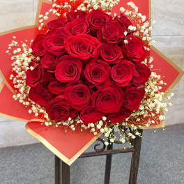 Round bouquet of red roses with white filler flowers wrapped in red and gold paper.
