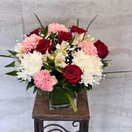 Bouquet of red roses, pink carnations, and white chrysanthemums in a glass vase