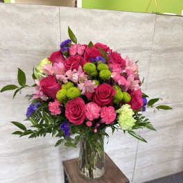 Bright pink roses, carnations, and mixed blooms in a clear glass vase on a small table