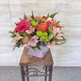 Mixed pink and orange flowers arranged in a square glass vase